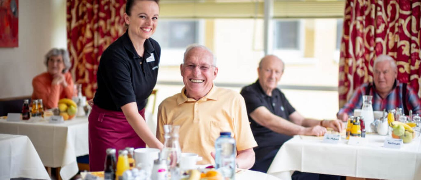 Servicekraft serviert freundlichem Senior Essen