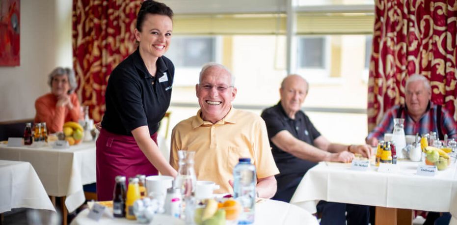 Servicekraft serviert freundlichem Senior Essen
