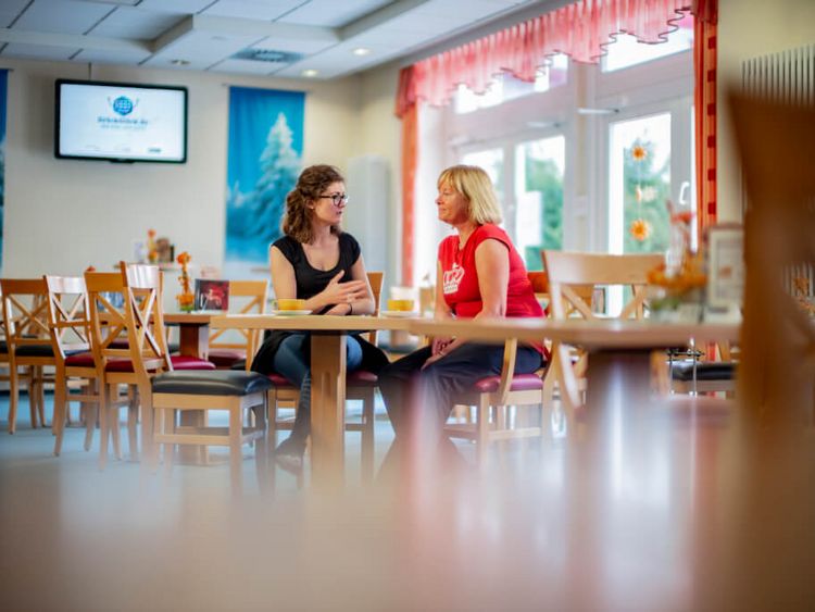 Servicemitarbeiterin spricht im Speisesaal mit Patientin
