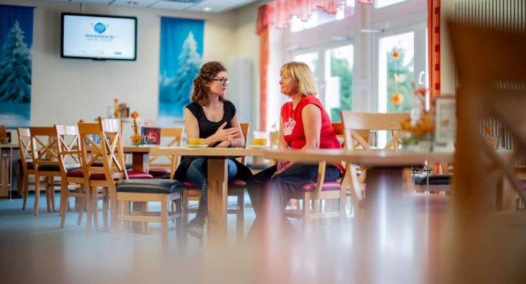 Servicemitarbeiterin spricht im Speisesaal mit Patientin