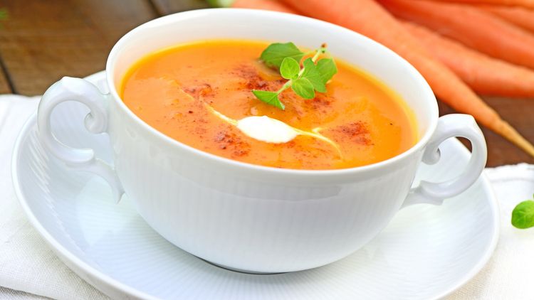 Karottensuppe mit Sahnehaube in einer antiken Suppentasse