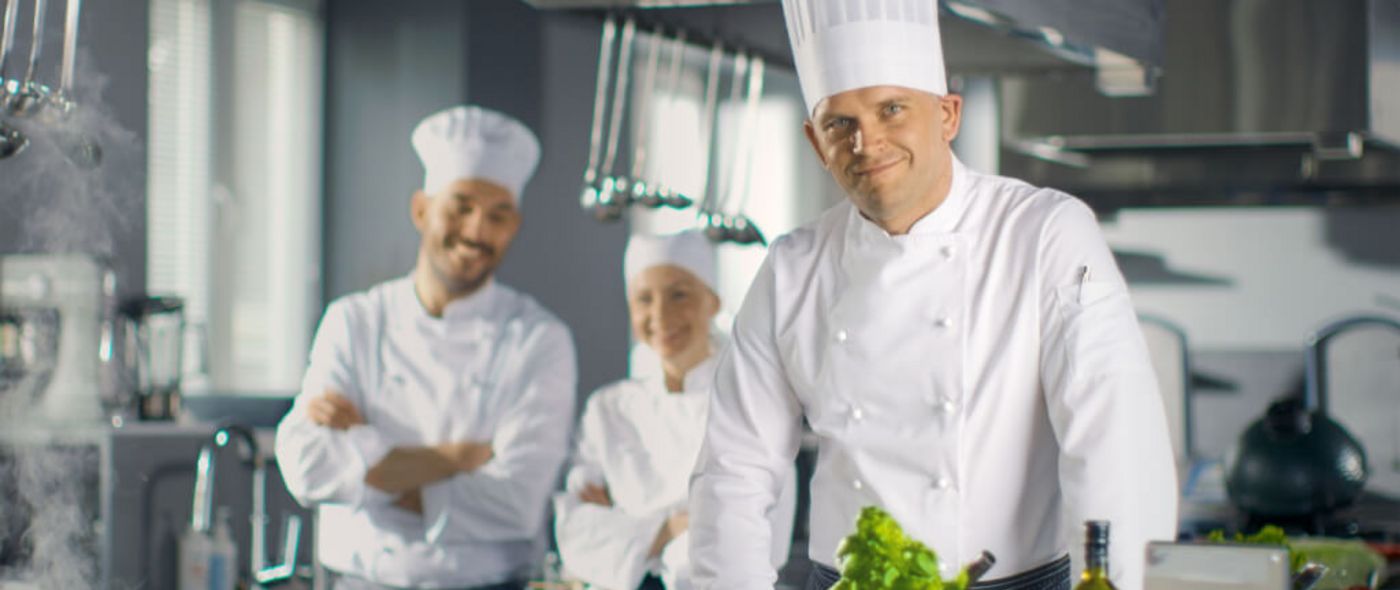 Küchenteam mit Chefkoch und Hilfen präsentiert Essen in einer Großküche