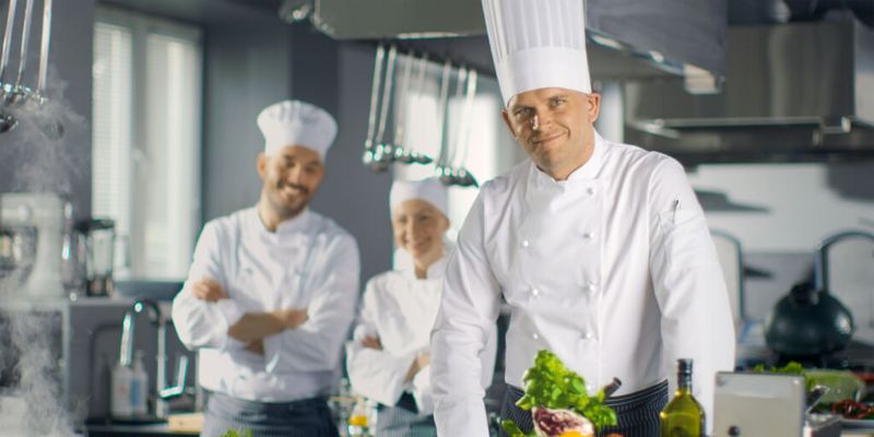 Küchenteam mit Chefkoch und Hilfen präsentiert Essen in einer Großküche