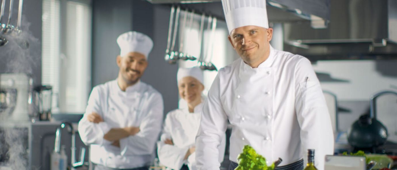 Küchenteam mit Chefkoch und Hilfen präsentiert Essen in einer Großküche