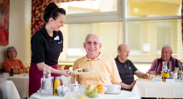 Servicemitarbeiterin serviert freundlichem Senior Essen