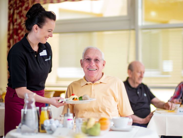 Servicemitarbeiterin serviert freundlichem Senior Essen