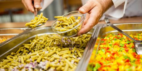 Koch füllt Gemüse am Buffet in eine kleine Schale