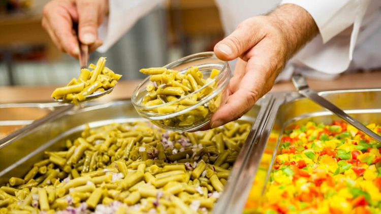 Koch füllt Gemüse am Buffet in eine kleine Schale
