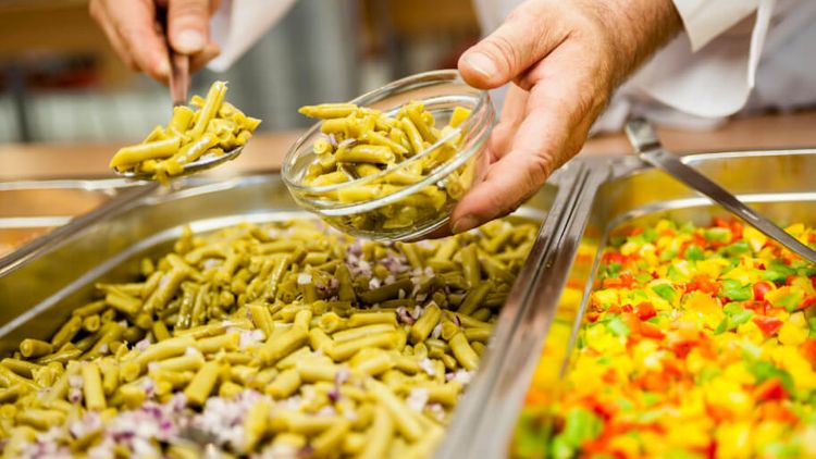 Koch füllt Gemüse am Buffet in eine kleine Schale